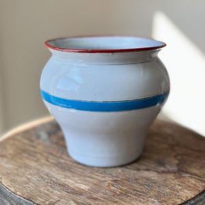 May include: White enamelware pitcher with a blue and red rim. The pitcher has a blue stripe around the middle.
