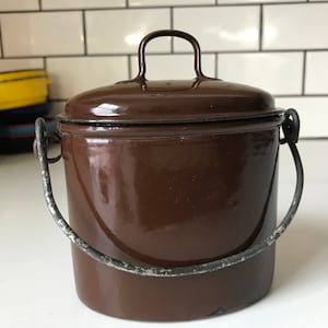 May include: A brown enamelware pot with a lid and a metal handle. The pot has a shiny finish and is in good condition.