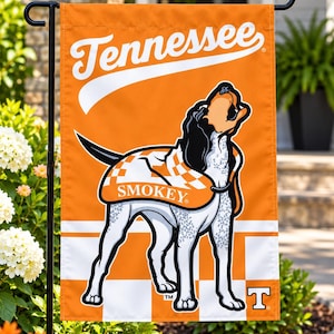 Op de afbeelding: Een rechthoekige oranje en witte tuin vlag met het woord Tennessee in witte schrijfletters bovenaan. Een afbeelding van een hond die een geruite deken draagt met het woord Smokey erop gedrukt, staat in het midden boven een wit T-logo.