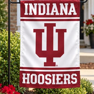 May include: A rectangular garden flag featuring a white center with a large crimson Indiana University IU logo. The top and bottom sections are crimson with the word INDIANA in white at the top and HOOSIERS in white at the bottom, all on a black metal stand.