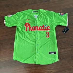 May include: A green baseball jersey with a red "Phanatic" logo and the number "3" on the front. The jersey has a white collar and white piping around the sleeves. The Nike swoosh logo is on the left chest.
