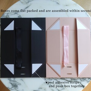 May include: Two flat-pack gift boxes, one black and one pink, with adhesive strips for assembly. The boxes are folded flat and have a ribbon loop on the top. The text on the image reads: "Boxes come flat packed and are assembled within seconds" and "peel adhesive strips and push box together".