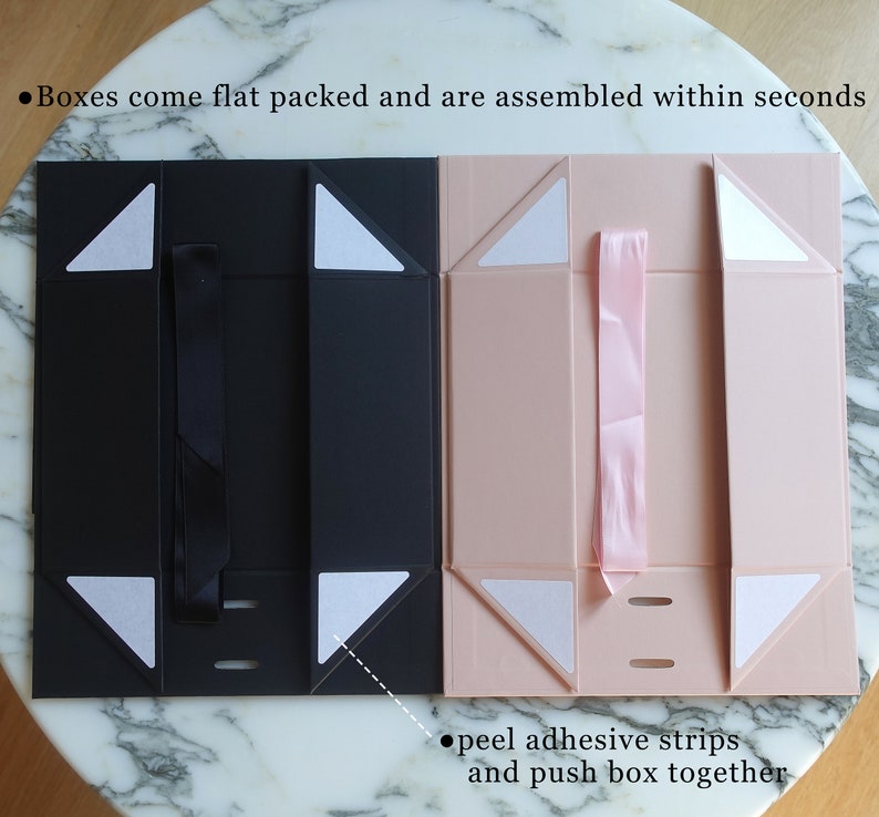 May include: Two flat-pack gift boxes, one black and one pink, with adhesive strips for assembly. The boxes are folded flat and have a ribbon loop on the top. The text on the image reads: "Boxes come flat packed and are assembled within seconds" and "peel adhesive strips and push box together".