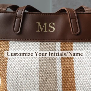 May include: A brown leather tote bag with a white and brown striped canvas bottom. The bag has gold initials "MS" on the front. The text "Customize Your Initials/Name" is printed below the initials.