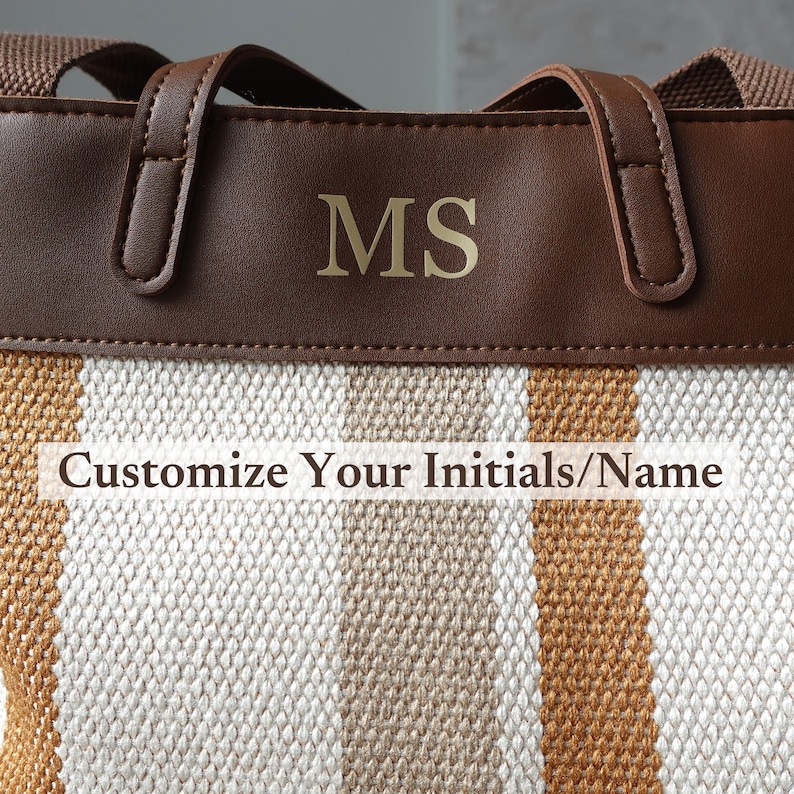 May include: A brown leather tote bag with a white and brown striped canvas bottom. The bag has gold initials "MS" on the front. The text "Customize Your Initials/Name" is printed below the initials.