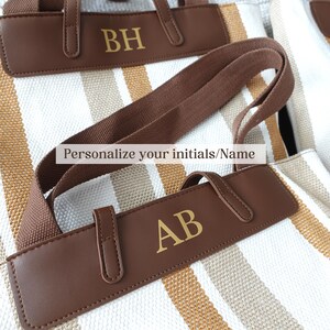 May include: Two striped canvas tote bags with brown leather handles and gold lettering. The top bag has the initials "BH" and the bottom bag has the initials "AB". The text "Personalize your initials/Name" is visible on the image.