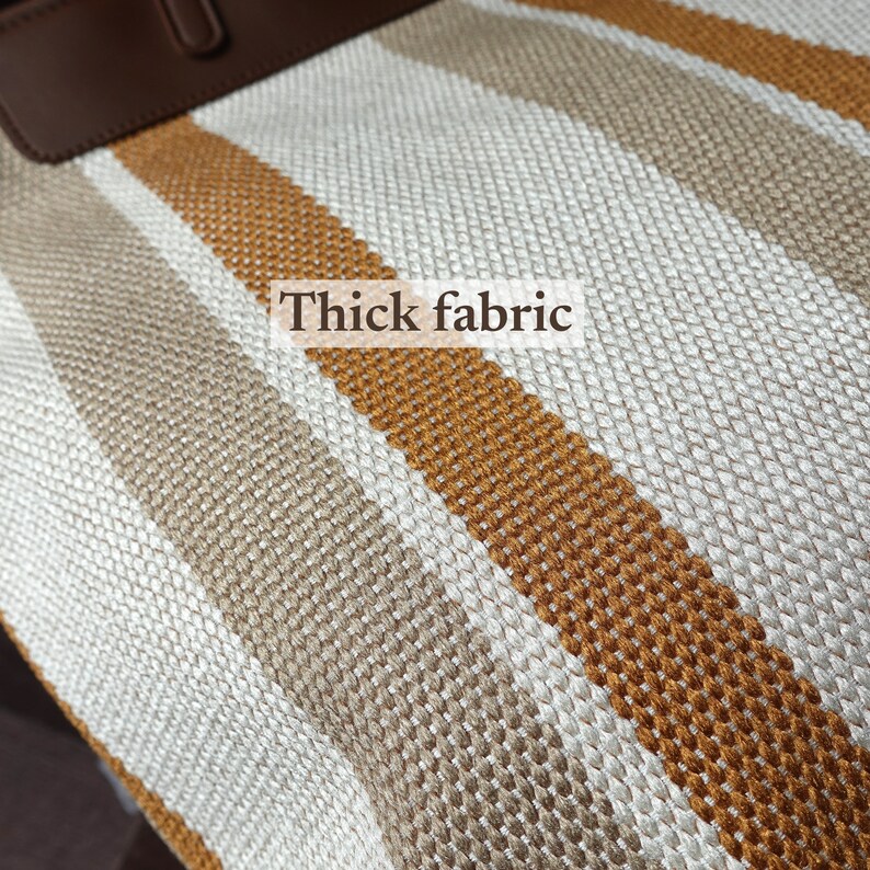 May include: Close-up of a striped fabric with thick, woven texture. The fabric is a combination of white, beige, and brown stripes.