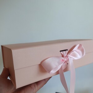 May include: A pale pink gift box with a satin ribbon tied in a bow. The box has a magnetic closure.