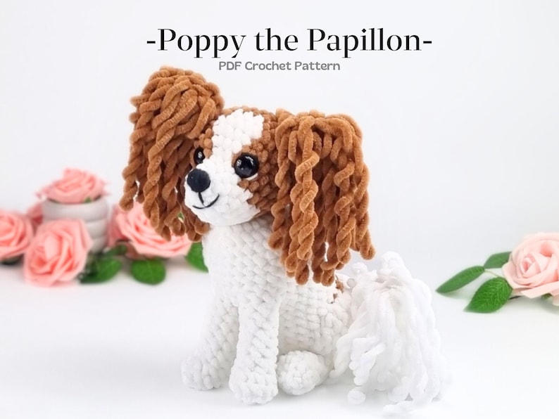May include: A handmade crochet dog in white, brown, and black. The dog has long, curly brown ears and a fluffy white tail. The text "-Poppy the Papillon-" and "PDF Crochet Pattern" are at the top.