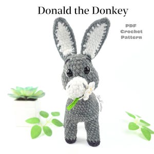 May include: A handmade crochet donkey toy in grey, white, and black, holding a white flower with a green stem. The donkey has large eyes and long ears. Text at the top reads "Donald the Donkey" and "PDF Crochet Pattern".