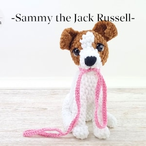 Könnte beinhalten: Ein gehäkeltes Jack-Russell-Terrier-Spielzeug mit braunem und weißem Fell, das eine rosafarbene Leine im Maul hält. Der Hund sitzt auf einer hellen Holzoberfläche. Der Text "Sammy the Jack Russell" steht über dem Hund.