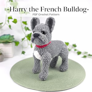 Könnte beinhalten: Ein graues gehäkeltes Amigurumi-Spielzeug eines französischen Bulldoggen mit rotem Halsband und weißen Markierungen. Das Spielzeug sitzt auf einem grünen Platzdeckchen. -Harry the French Bulldog- PDF Häkelanleitung
