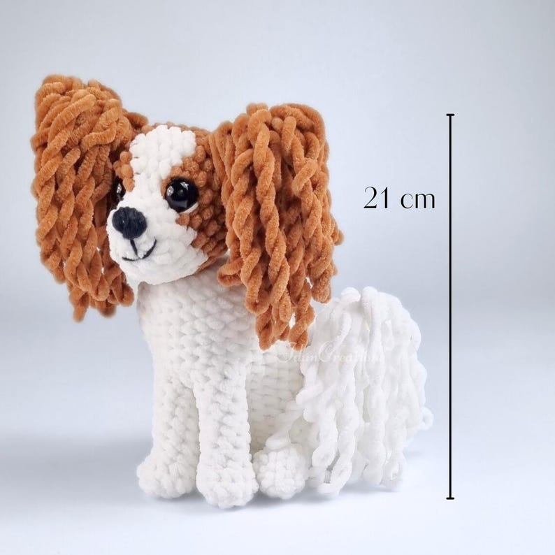 May include: A handmade, plush Cavalier King Charles Spaniel dog, primarily white with brown and tan accents. The dog is approximately 21 cm tall. The dog has large, floppy ears and a fluffy tail, with black eyes and nose.