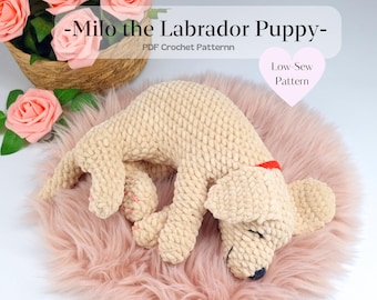 May include: A crocheted Labrador puppy in a sleeping position, lying on a pink faux fur rug. The puppy is beige with a red collar and a black nose. The text "-Milo the Labrador Puppy-" and "Low-Sew Pattern" are visible.