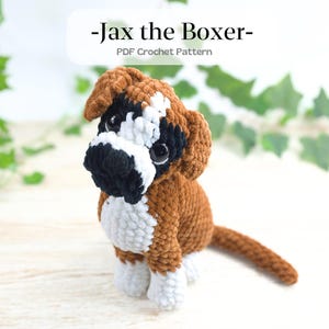 Peut inclure: Un chien boxer au crochet, marron, blanc et noir. Le chien est assis avec une courte queue. Le texte "-Jax the Boxer- PDF Crochet Pattern" est en haut de l'image. Le fond est orné de verdure.