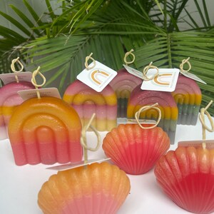 May include: Assortment of colorful hand-crafted candles in the shape of seashells and rainbows. The candles are made with natural soy wax and have a subtle, sweet scent.