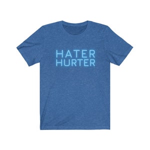 May include: A blue heather t-shirt with the words "HATER HURTER" in a light blue neon font.