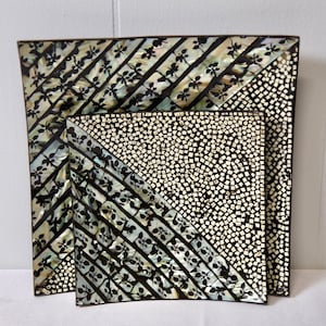 May include: Two decorative square trays. The larger tray has a diagonal pattern of black leaves on a light background, with a mosaic of small white squares on the other half. The smaller tray has a similar design.