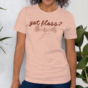 May include: A pink t-shirt with the text "got floss?" in brown lettering. The shirt features a graphic of a needle and thread.