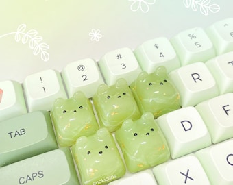 May include: A set of five green and gold keycaps featuring a bear design. The keycaps are arranged on a green and white keyboard.