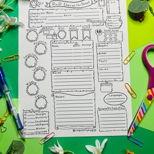 May include: A black and white D&D character sheet with fillable sections for stats, attacks, and notes. The sheet includes spaces for character name, class, race, and other game-related information. The sheet is surrounded by colorful office supplies.