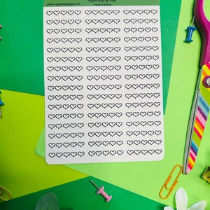 May include: A sheet of stickers with numerous black heart outlines, labeled "Hearts Rating" by "Roguishly by Gigi." The stickers are on a white background, surrounded by green and yellow paper, with office supplies like push pins and paper clips.