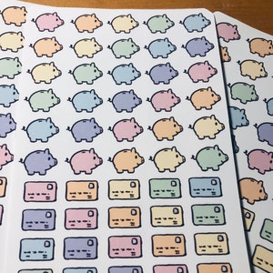May include: A sheet of pastel colored stickers featuring piggy banks and credit cards. The stickers are arranged in rows and columns on a white background. The text "etsy.com/shop/roguishlybygigi @roguishlybygigi" is printed at the bottom of the sheet.