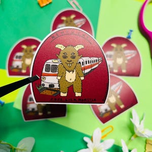 May include: A collection of stickers featuring a cartoon monster with a train graphic. The stickers are red with white and brown details, and the text "Pope Lick Monster" is visible. The stickers are on a green and yellow background with paper clips and flowers.