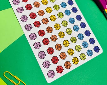 May include: A sheet of colorful D20 dice stickers in various colors, including red, orange, yellow, green, blue, and purple. Each sticker features a 20-sided die design with the number 20. The sheet is on a green surface with office supplies.