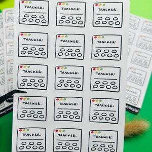 May include: A sheet of 15 colorful habit tracker stickers. Each sticker has a black border and a white interior with five circles and a line. The stickers are labeled "TRACKER:" with a small traffic light icon in the top left corner.