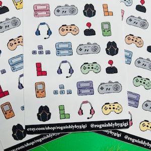 May include: Sheets of stickers featuring various gaming-related icons, including game controllers, headsets, and handheld consoles. The stickers are in a doodle style with a variety of colors and shapes. The text "etsy.com/shop/roguishlybygigi" is visible.