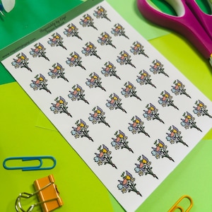 May include: A sheet of stickers featuring a repeating pattern of small, colorful flower bouquets. The stickers have a white background and are surrounded by office supplies, including scissors, paper clips, and a push pin. The text "Requishly by Gigi" is visible.