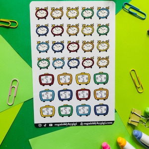 May include: A sheet of colorful alarm clock stickers. The stickers are in various colors, including red, yellow, blue, green, and orange. The alarm clocks are all in the same style, with a round face and a bell on top. The stickers are perfect for adding a touch of fun to your planner or journal.