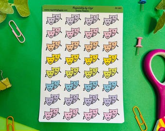 May include: A sheet of stickers featuring cartoon drama masks in various colors: pink, peach, yellow, blue, and purple. The stickers are on a white background, with the text "Roguishly by Gigi Drama Theatre" and "OC-001". The background is green.