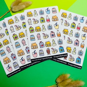 May include: Three sheets of stickers with various illustrations of drinks and food. The stickers are white with black outlines and feature colorful illustrations of juice boxes, cans, cups, and cherries. The text on the stickers reads "Juice" and "Shake". The stickers are arranged in rows and columns on a green background.