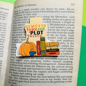 Könnte beinhalten: Ein farbenfrohes Lesezeichen mit einem Kürbis, einer Tasse Kaffee und gestapelten Büchern. Das Lesezeichen trägt den Text "Pumpkin Spice and Plot Twists".