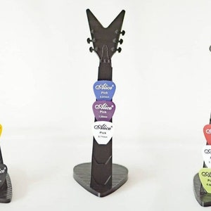 Puede incluir: Tres soportes negros para púas de guitarra, cada uno con forma de guitarra. Cada soporte muestra tres púas de guitarra de diferentes colores, con el logotipo "Alice Pick" y medidas de grosor en milímetros.