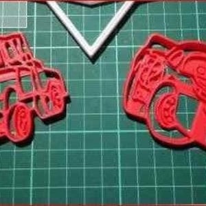 Puede incluir: Dos cortadores de galletas de plástico rojo con forma de coches de dibujos animados. Los cortadores están sobre una estera de corte verde.