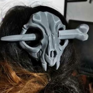 Puede incluir: Una pinza para el pelo de color gris en forma de cráneo impresa en 3D con un pasador en forma de hueso. El cráneo tiene un diseño detallado y es un accesorio único para el cabello.