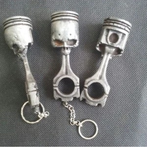 Puede incluir: Tres llaveros de plata en forma de calavera hechos de bielas metálicas. Cada llavero tiene un anillo de plata unido a la parte inferior.