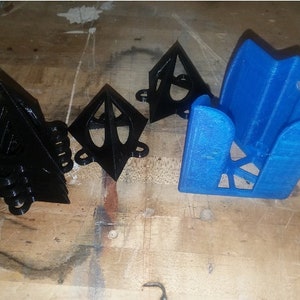 May include: Three black 3D printed geometric shapes and a blue 3D printed holder. The shapes are triangular and have a textured surface. The holder is rectangular and has a hollow interior.