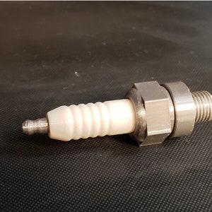 以下が含まれることがあります： 白いセラミック絶縁体を持つ銀色のスパークプラグ。スパークプラグはねじ切り端と六角ナットを持っています。