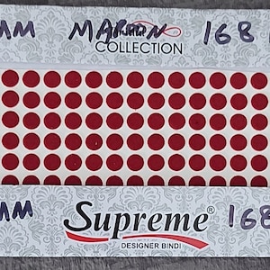 May include: A sheet of 168 red 5 mm round adhesive bindis. The bindis are arranged in a grid pattern on a white background. The packaging says "Supreme Designer Bindi" and "Maroon Collection".
