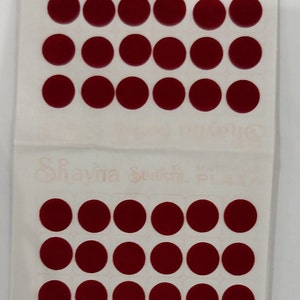 Puede incluir: Una hoja de 36 pegatinas redondas de bindi adhesivas. La hoja está doblada por la mitad y el texto "Shayna Studio" es visible en la mitad inferior de la hoja.