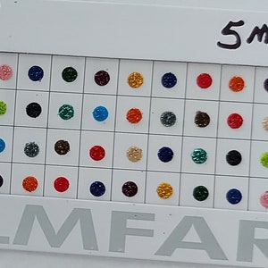 Può includere: Un cartoncino bianco con il testo "Roop Palak Fancy Bindi" e "5mm" stampato su di esso. Il cartoncino presenta una griglia di 48 piccoli bindis rotondi e colorati. I bindis sono disposti in file e colonne, con ogni fila che contiene 8 bindis. I bindis sono di vari colori, tra cui rosso, verde, blu, nero e argento. Il cartoncino presenta anche una piccola statua di un premio d'argento.