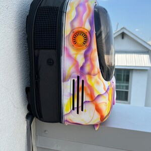 May include: A black backpack with a colorful, abstract design. The backpack has a clear bubble on the front and a mesh pocket on the side.