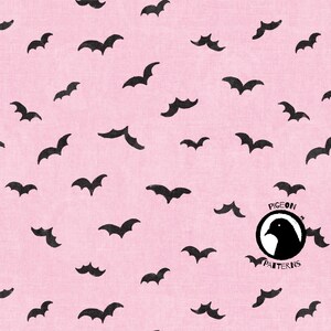 Op de afbeelding: Roze stof met een herhaald patroon van zwarte vleermuis silhouetten. De vleermuizen zijn in verschillende maten en posities, wat een grillig en griezelig ontwerp creëert. De stof heeft een licht getextureerde uitstraling. Het logo "PIGEON PATTERNS" staat rechtsonder.
