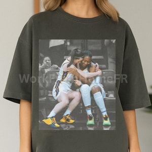 May include: Dark gray oversized t-shirt featuring a grayscale image of two athletes embracing. The image shows the athletes in their sports uniforms, seated on a bench. The t-shirt is a casual, comfortable style.