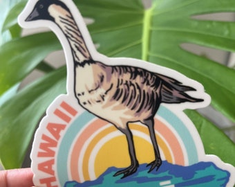Könnte beinhalten: Ein Aufkleber mit einer Cartoon-Illustration einer Nene-Gans, dem Staatsvogel von Hawaii, die auf einem felsigen Vorsprung steht, mit einem Sonnenuntergang dahinter. Der Aufkleber trägt die Aufschrift "HAWAII" und "NENE".