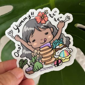 May include: A cartoon illustration of a girl with gray hair and a pink flower in her hair. She is holding a fork in each hand and has a happy expression on her face. The text "Yummy!" and "Ono!" are written on the sticker. The girl is surrounded by various foods, including pancakes, sushi, and a pineapple.